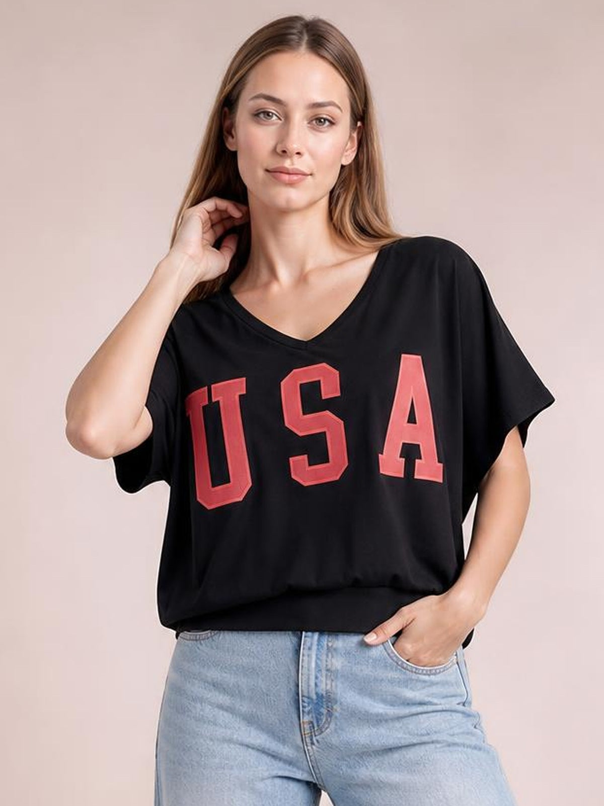 Model poses in a black USA notched short-sleeve T-shirt with a relaxed silhouette, V-neckline, and bold red lettering, paired with light-wash jeans.