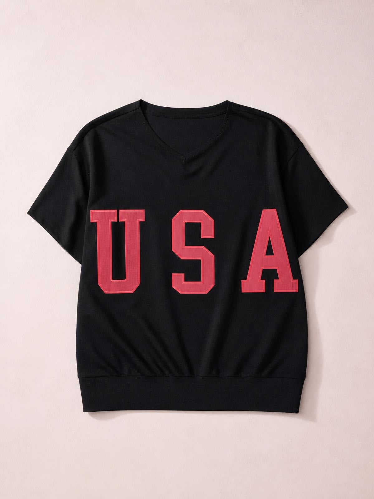 A black USA short sleeve T-shirt lies flat, featuring a notched V-neck, relaxed silhouette, and bold red collegiate-style lettering across the front.