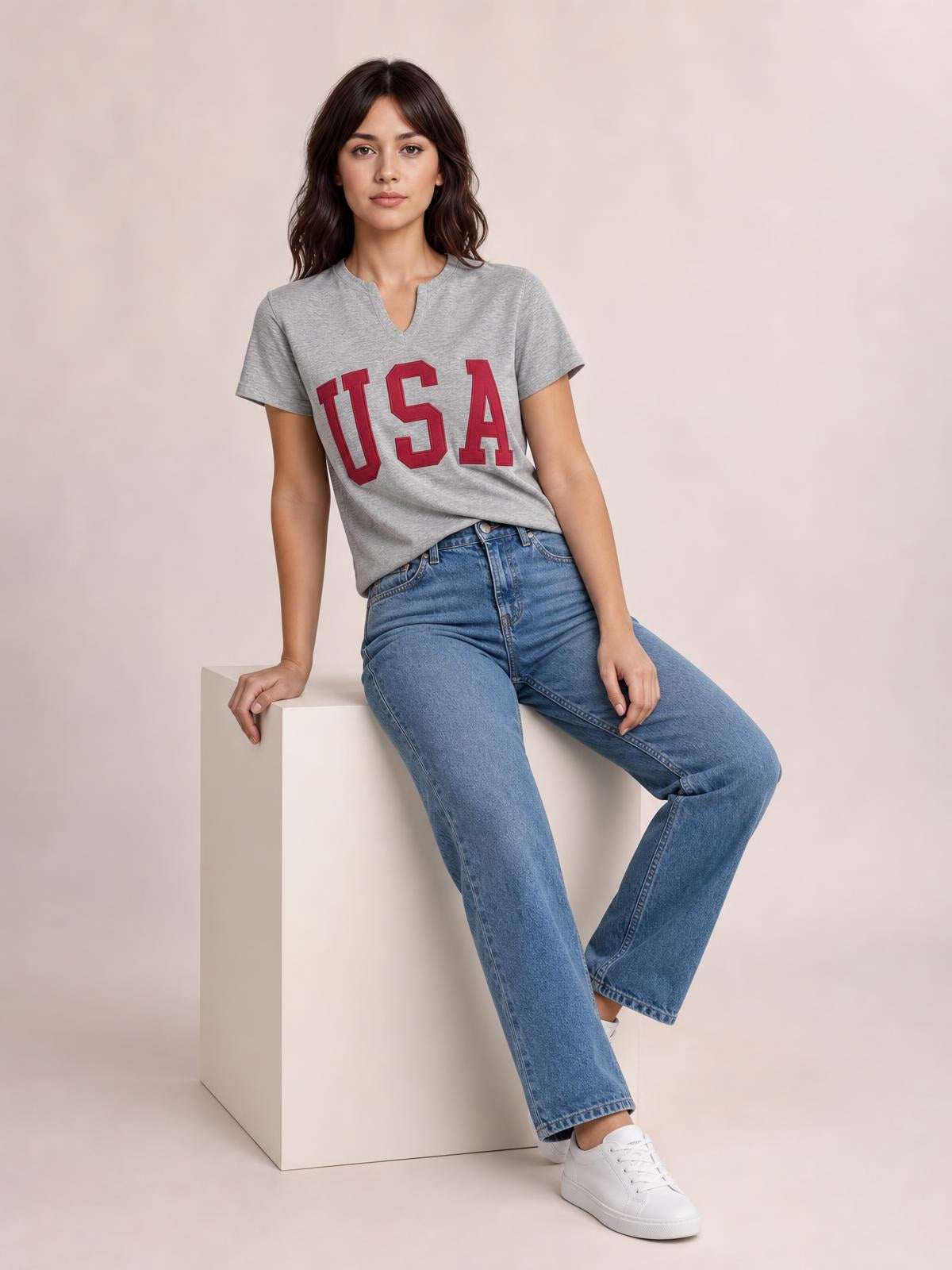 A model sits wearing a gray USA notched short sleeve T-shirt with bold red lettering, a relaxed silhouette, and a casual split neckline.