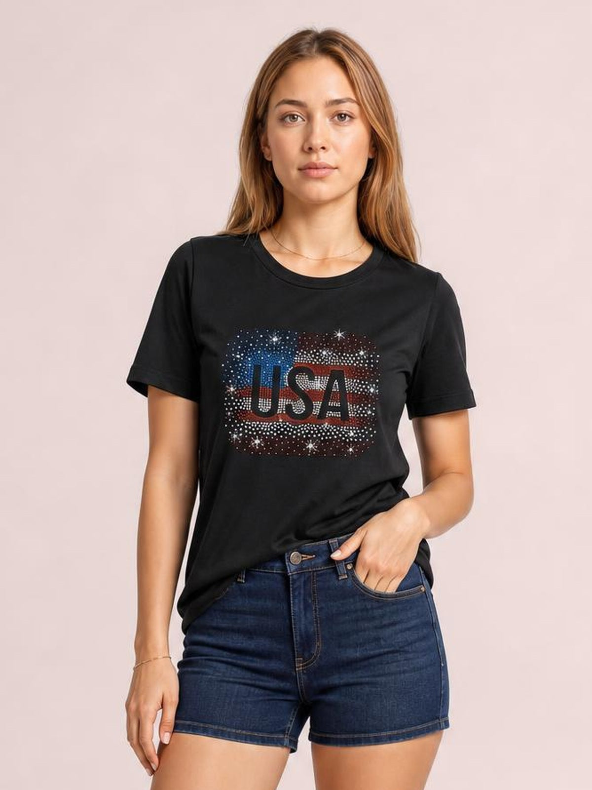 Model wears a black USA rhinestone round-neck T-shirt with short sleeves and a relaxed silhouette, paired with denim shorts and one hand in a pocket.