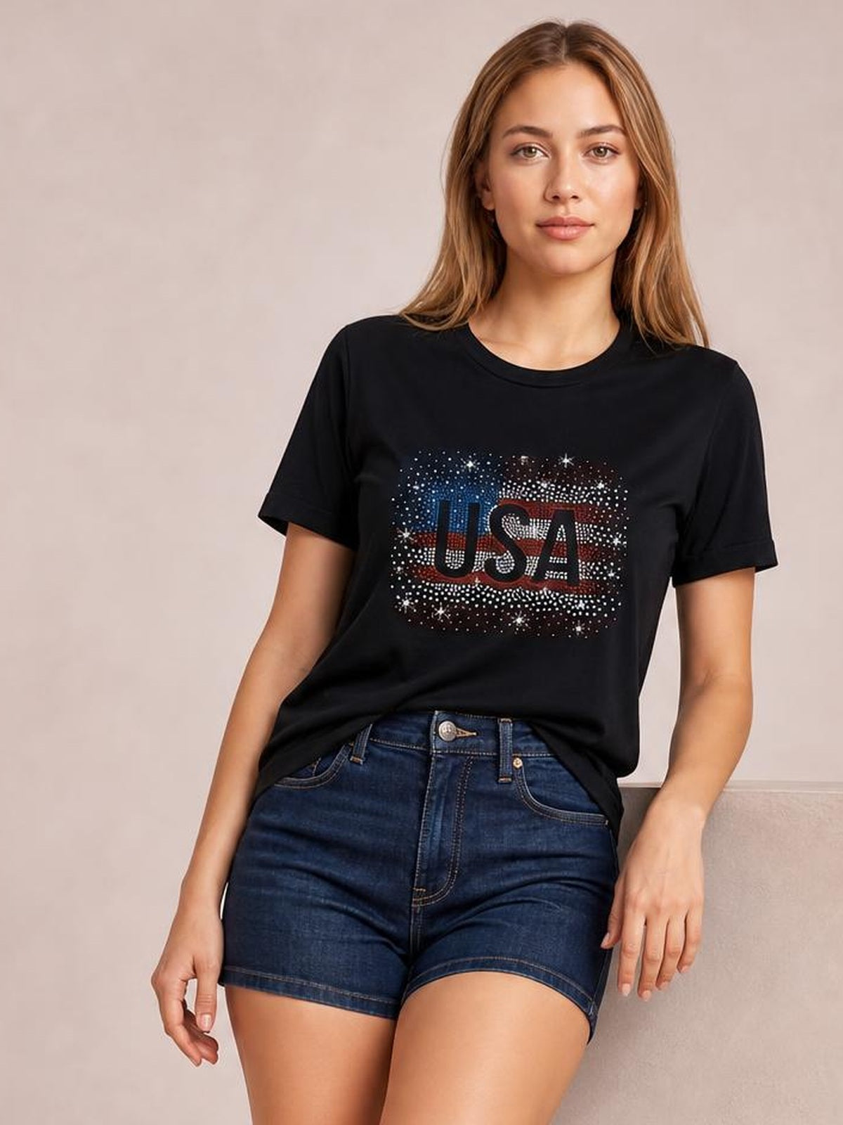A model leans casually in a black round-neck short-sleeve T-shirt with a relaxed silhouette and sparkling USA rhinestone graphic.