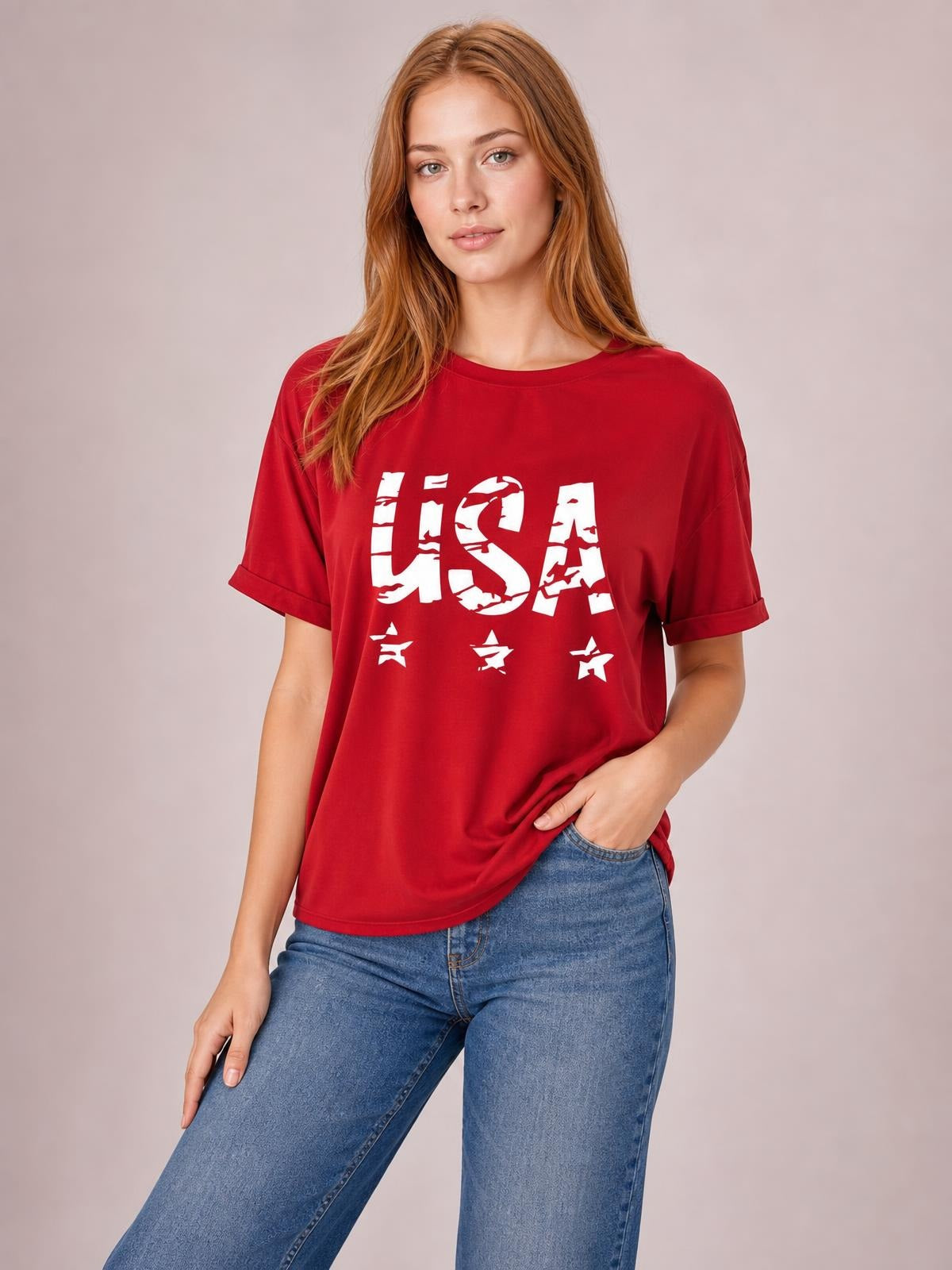 Model poses in a red USA round neck short sleeve T-shirt with a classic fit, bold white lettering and star graphics, rolled sleeve cuffs, and a relaxed silhouette.