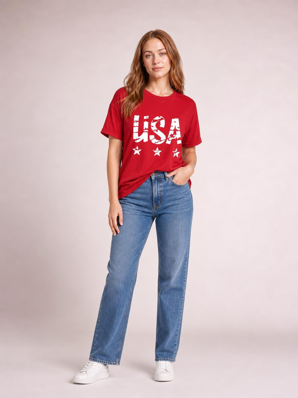 A model stands in a red USA round neck short sleeve T-shirt with a classic fit, bold white lettering and stars, one hand resting in her jeans pocket.