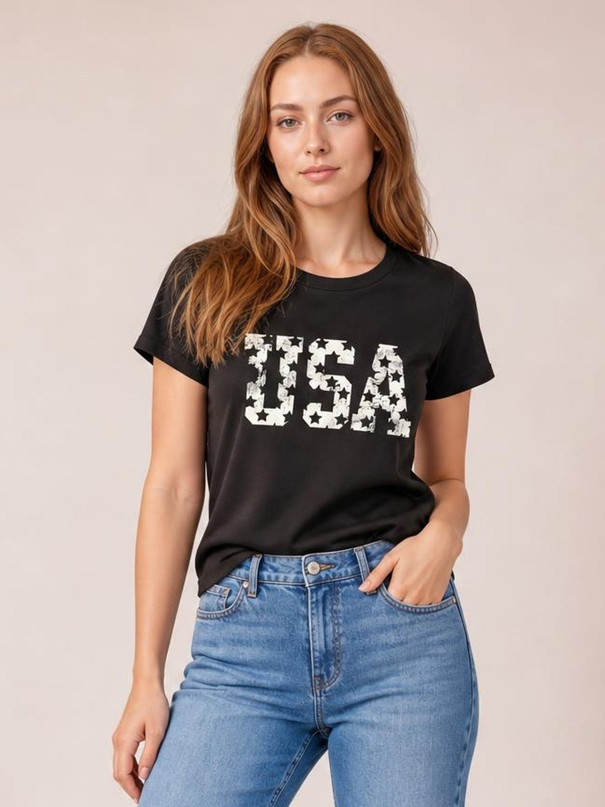 Model wearing a black USA round neck short sleeve T-shirt with a bold white star-print graphic and relaxed silhouette, standing with one hand in her jeans pocket.