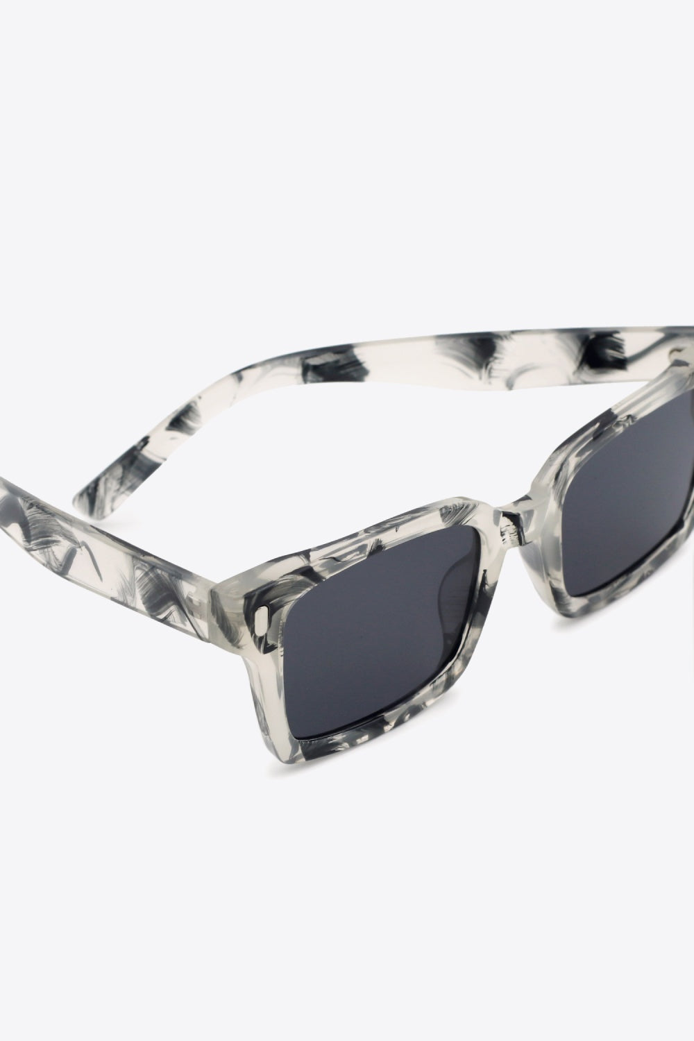 Close-up of UV400 polycarbonate square sunglasses with translucent marbled frames, dark lenses, broad softly rounded-square silhouette, and defined temples.