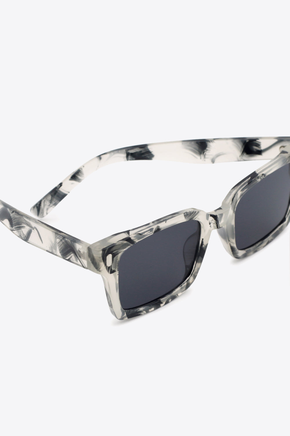 Close-up of UV400 polycarbonate square sunglasses with translucent marbled frames, dark lenses, broad softly rounded-square silhouette, and defined temples.