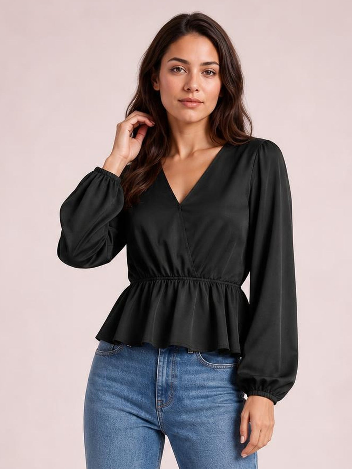Model poses in a black V-neck peplum blouse with voluminous balloon sleeves, gathered cuffs, a defined waist, and flared hem over blue jeans.