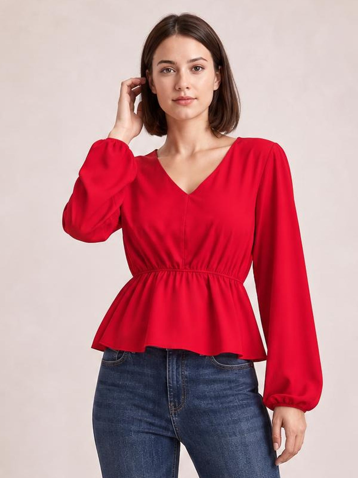 A woman poses in a red V-neck peplum blouse with voluminous balloon sleeves, gathered cuffs, fitted waist, and flared hem.