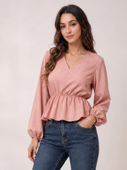 Model wearing a pink V-neck peplum blouse with long balloon sleeves, gathered waist, elastic cuffs, and a flared hem, posing with one hand in her jeans pocket.