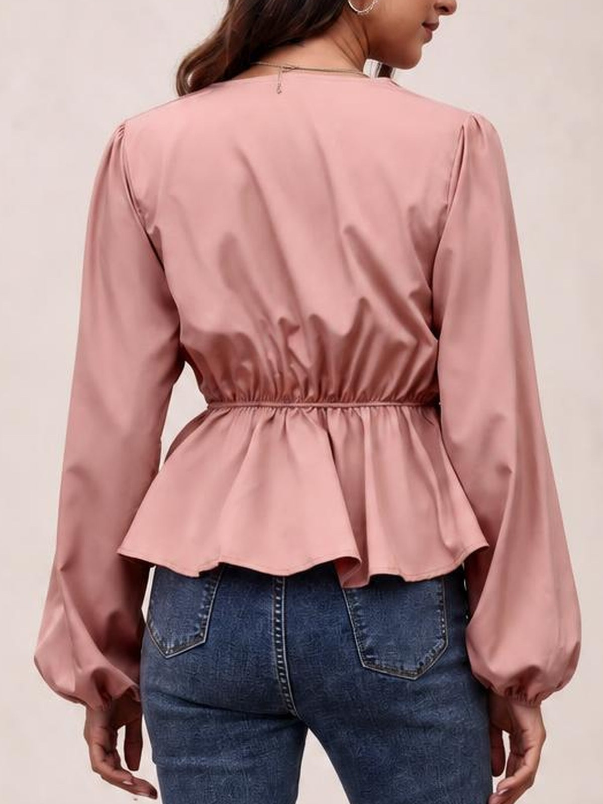 A model wears a pink peplum blouse from the back, showing voluminous balloon sleeves with gathered cuffs and a cinched, gathered waist.