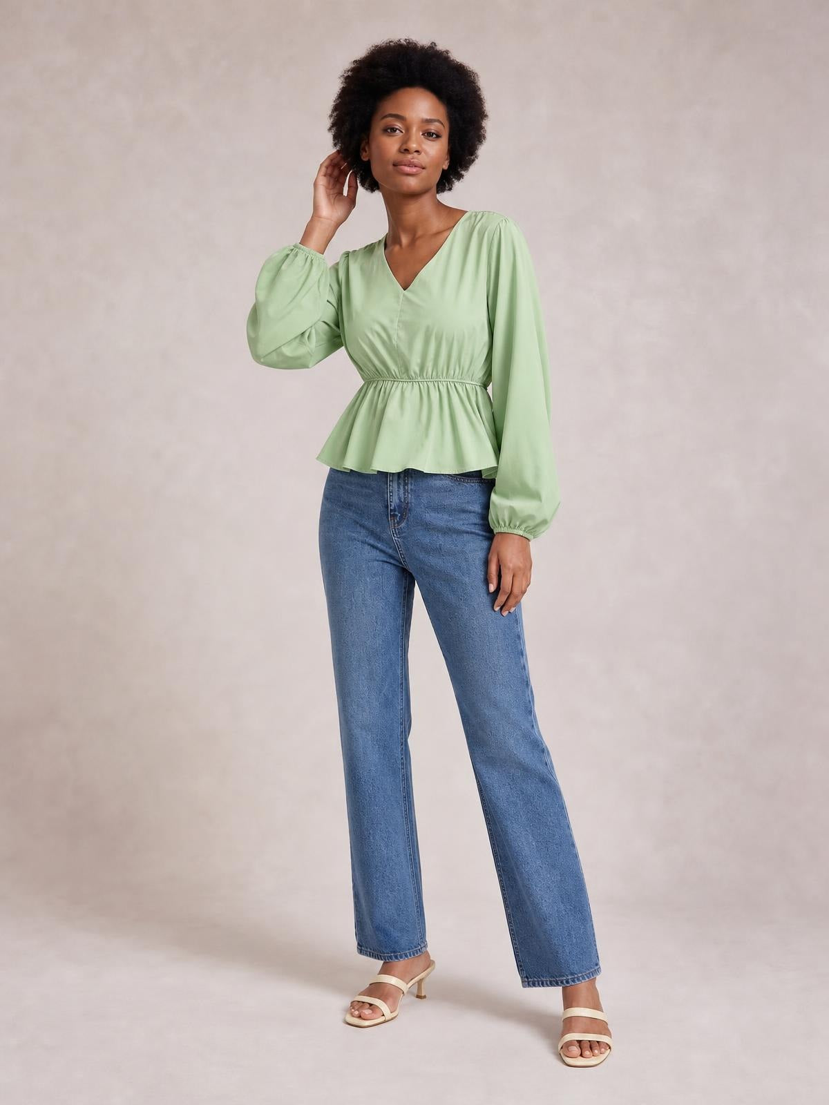 Model poses in a light green V-neck peplum blouse with gathered waist, voluminous balloon sleeves, and elasticized cuffs.