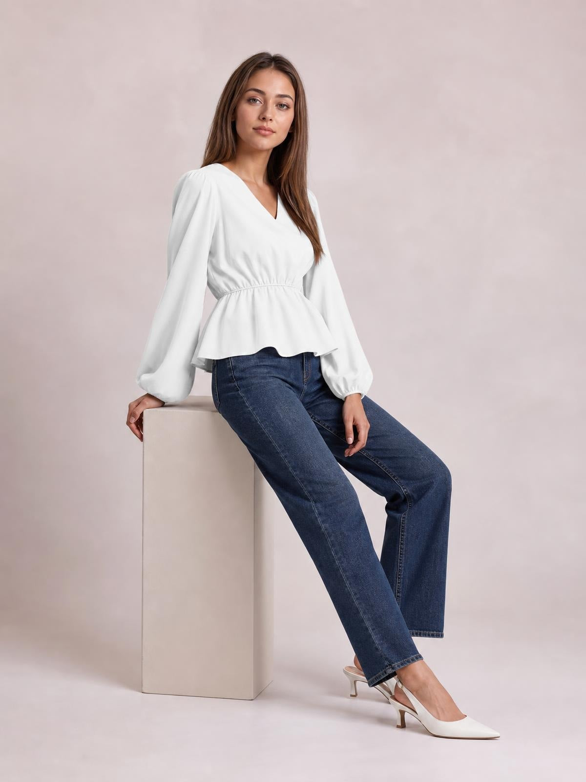 A seated model wears a white V-neck peplum blouse with voluminous balloon sleeves, gathered waist, and a flared hem creating a defined silhouette.