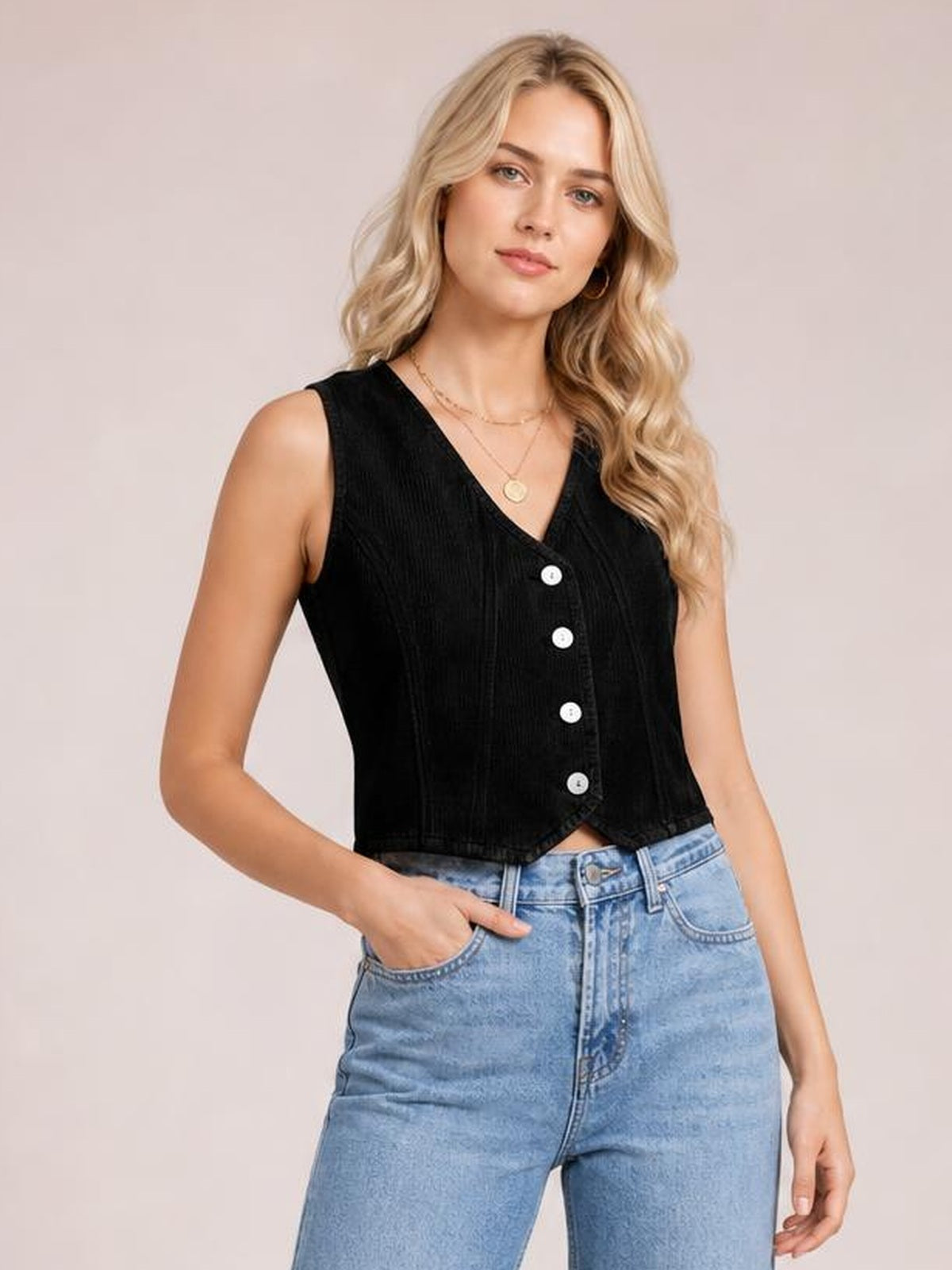 A model poses in a black sleeveless V-neck button-down vest with a fitted, cropped silhouette and visible front buttons, paired with light-wash jeans.