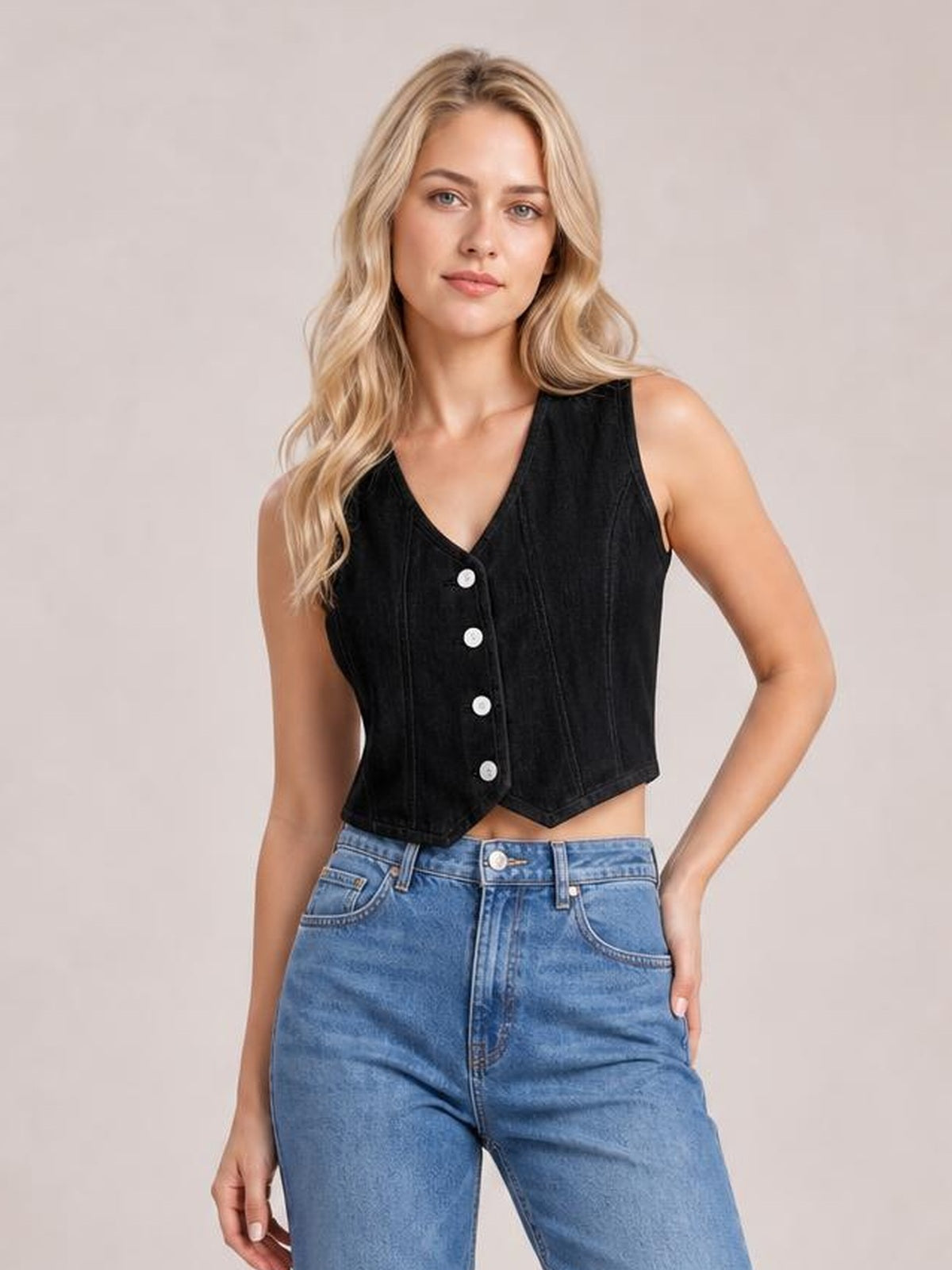 A model wears a black denim vest with a V-neck, sleeveless cut, front button-down closure, vertical seams, fitted cropped silhouette, and pointed hem.