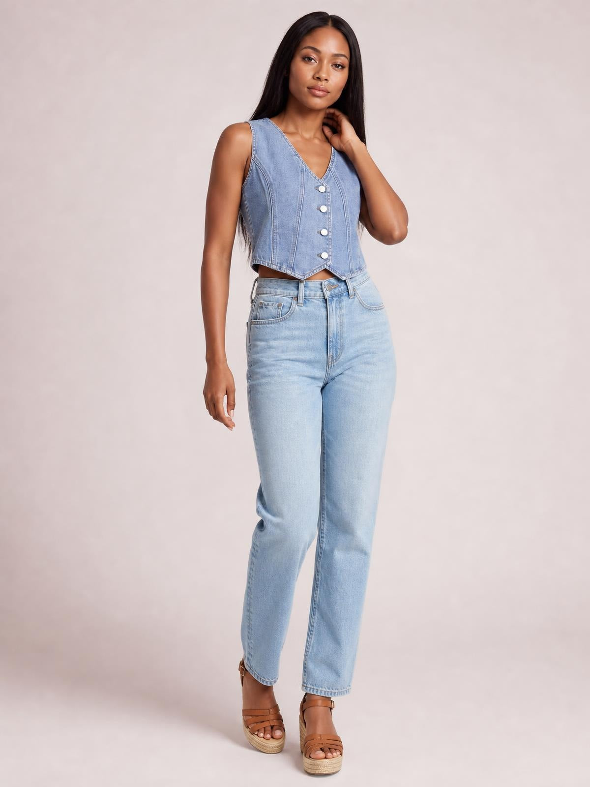 Model poses in a light blue denim vest with a V-neck, sleeveless design, button-down front, vertical seaming, and a fitted cropped silhouette.