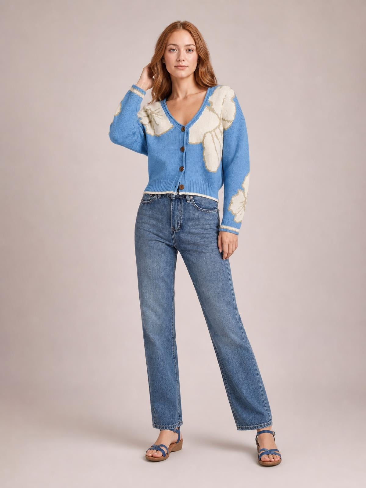 Model poses in a blue V-neck button-down knit cardigan with cream floral color-blocking, long sleeves, seam detail, ribbed trim, and a cropped silhouette.