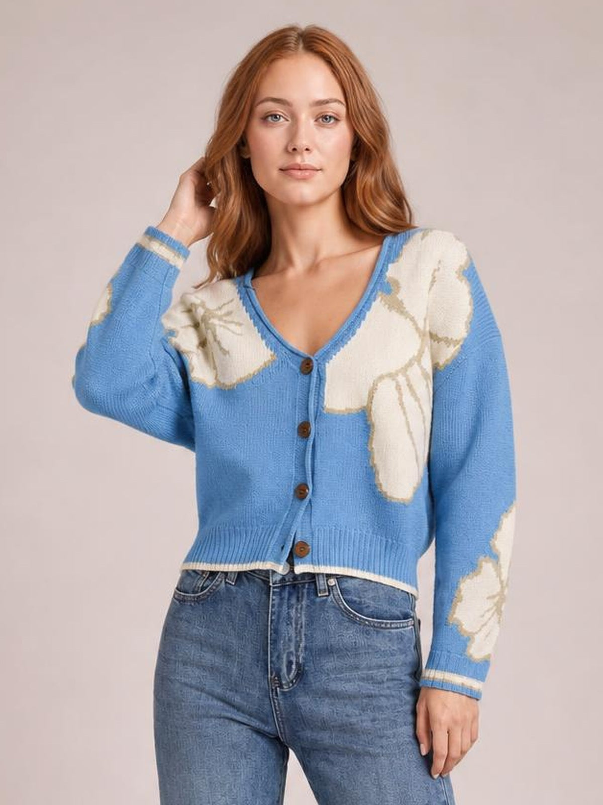 Model poses in a blue V-neck button-down knit cardigan with cream floral panels, long sleeves, ribbed trim, seam detailing, and a cropped silhouette.