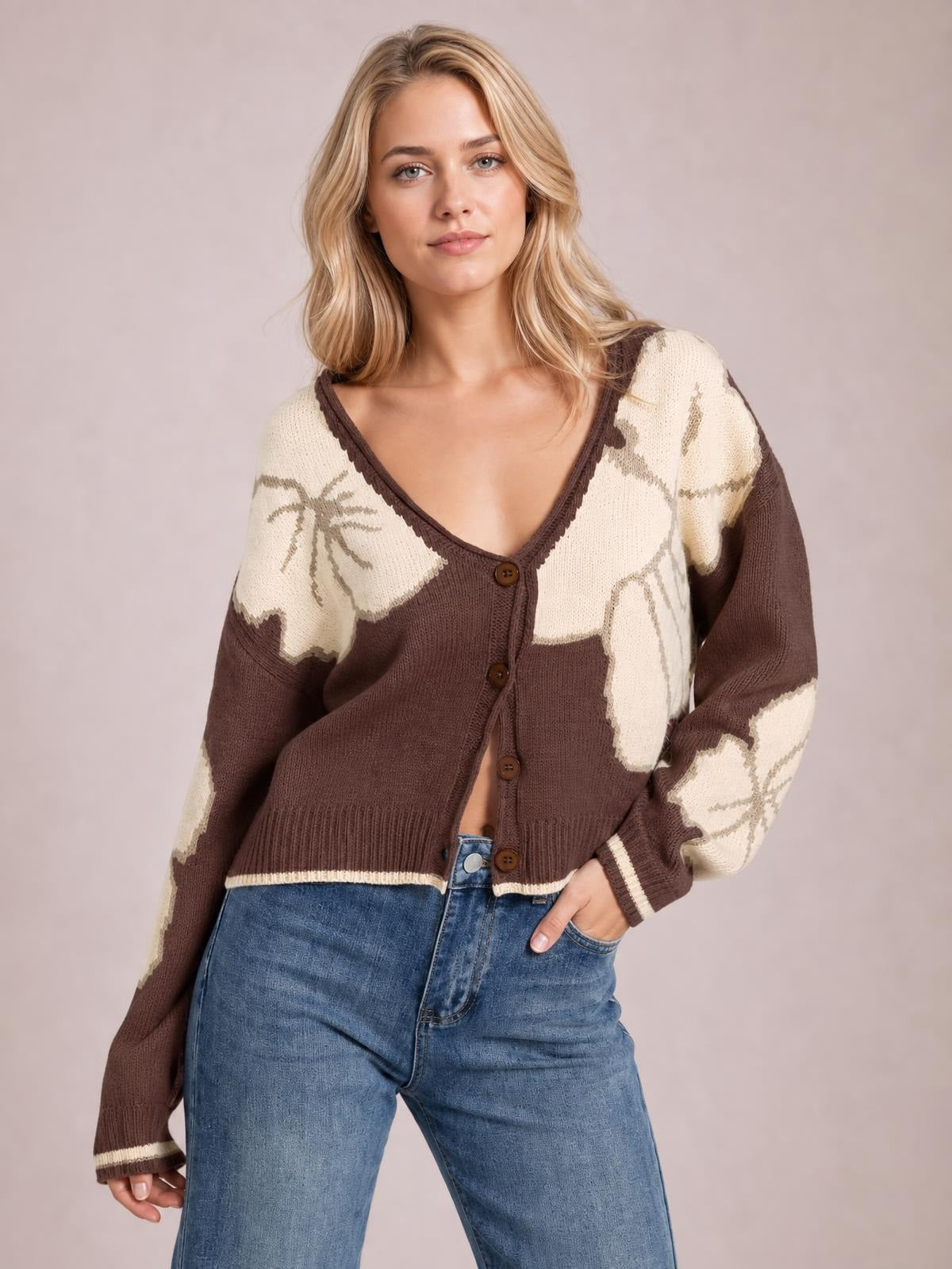 Model poses with one hand in her jeans pocket wearing a brown and cream V-neck button-down knit cardigan with contrast sleeves, ribbed hem, and relaxed fit.