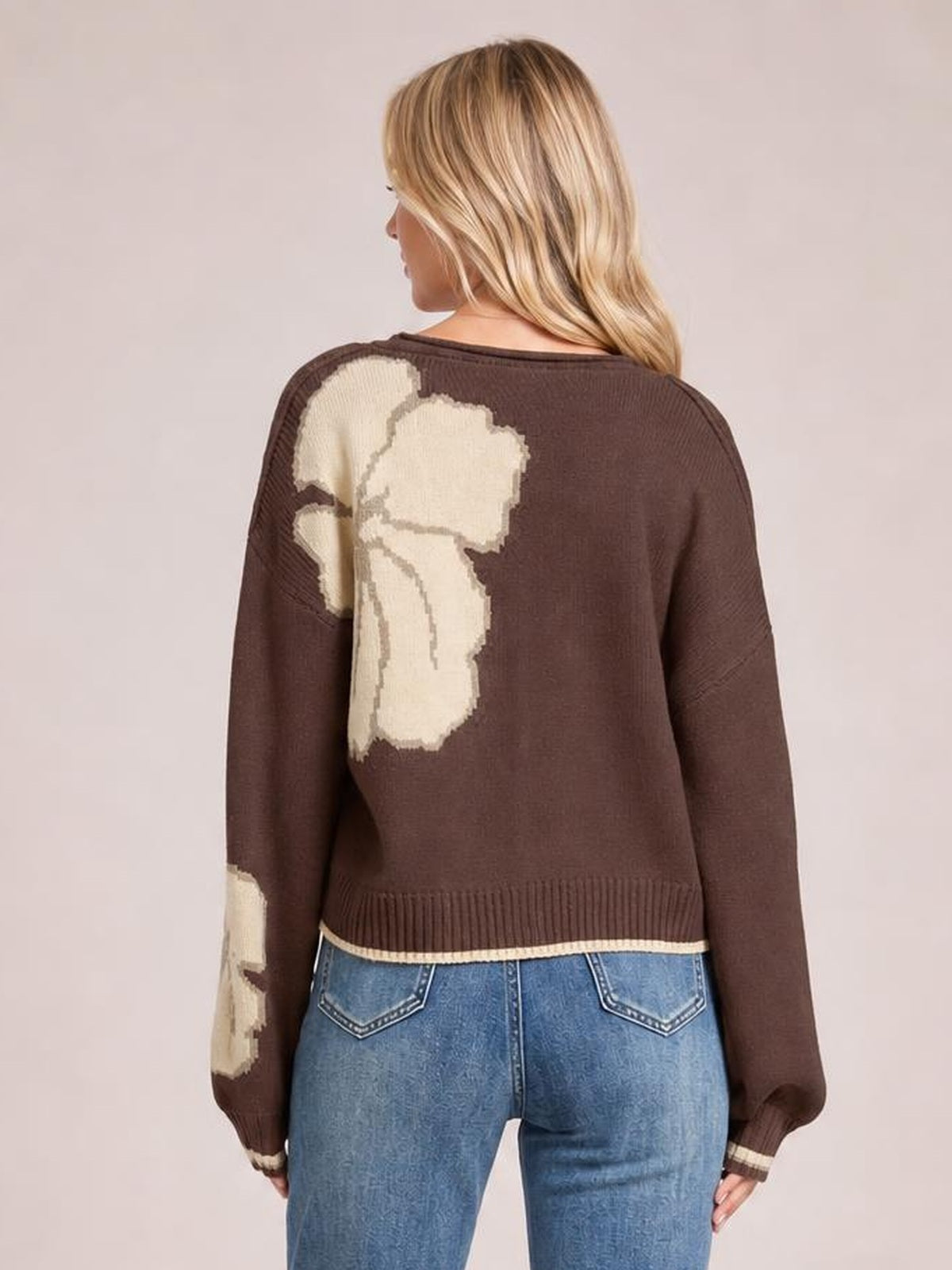 Back view of a woman wearing a brown knit cardigan with cream floral color-block detail, long sleeves, ribbed hem and cuffs, paired with jeans.