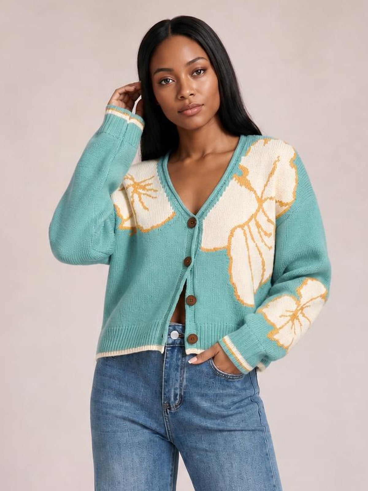 Model poses in a turquoise V-neck button-down knit cardigan with floral contrast panels, seam detail, ribbed cuffs and hem, and a relaxed fit.