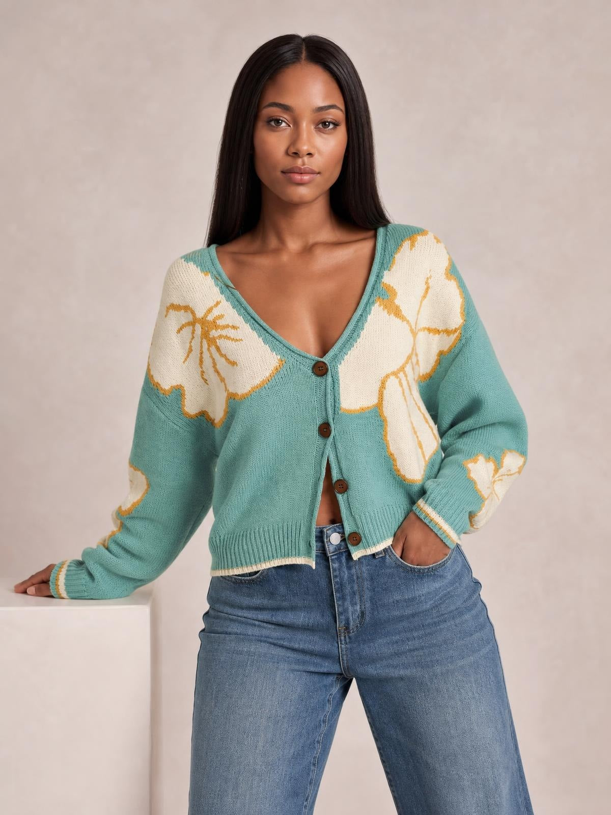 Model wears a teal and cream V-neck button-down knit cardigan with floral color-blocking, seam detail, ribbed cuffs and hem, and a cropped silhouette.