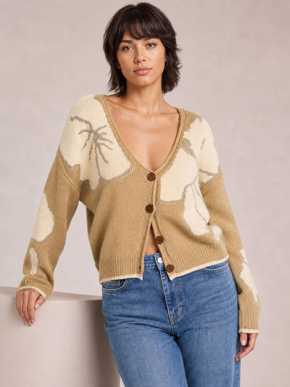 Model poses in a tan and cream V-neck button-down knit cardigan with contrast abstract pattern, seam detailing, long sleeves, and a relaxed cropped silhouette.