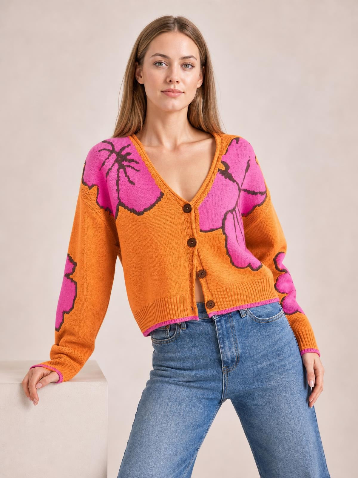 Model wears an orange and pink patterned knit cardigan with a V-neck, button-down front, long sleeves, ribbed trim, and a cropped silhouette.