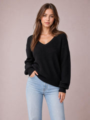 Model poses in a black V-neck drop shoulder sweater with a relaxed oversized silhouette, ribbed cuffs and hem, and textured knit construction.