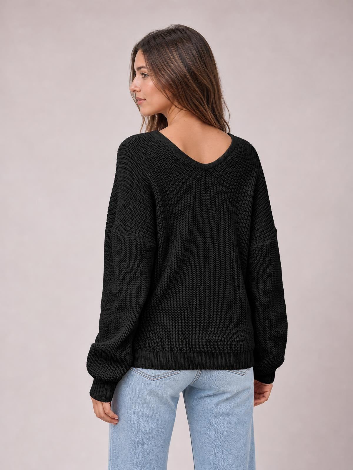 Model looks over her shoulder wearing a black V-neck drop shoulder sweater with a relaxed oversized fit, textured knit, and ribbed cuffs and hem.