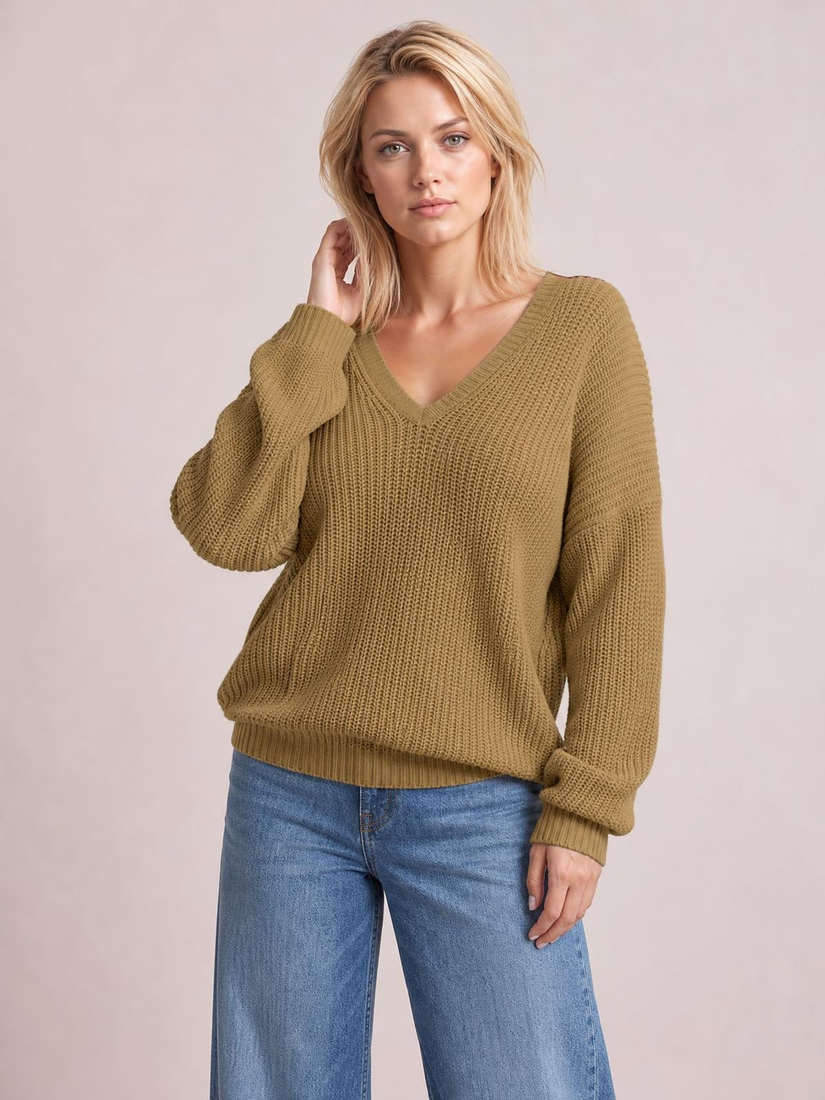 Model poses in a relaxed stance wearing a brown V-neck drop shoulder sweater with a chunky knit texture, long sleeves, ribbed cuffs, and a relaxed silhouette.