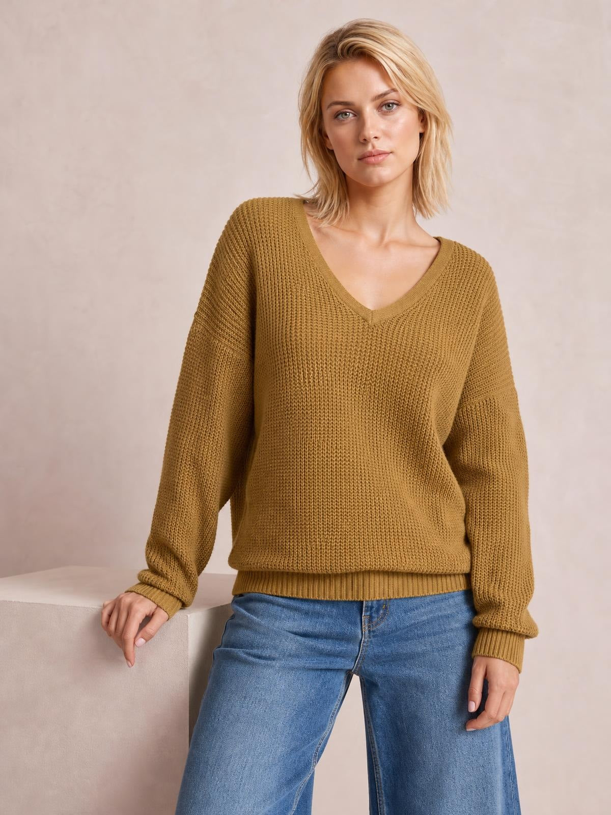 Model wearing a mustard V-neck drop shoulder sweater with a relaxed silhouette, ribbed trim, long sleeves, and textured knit construction.