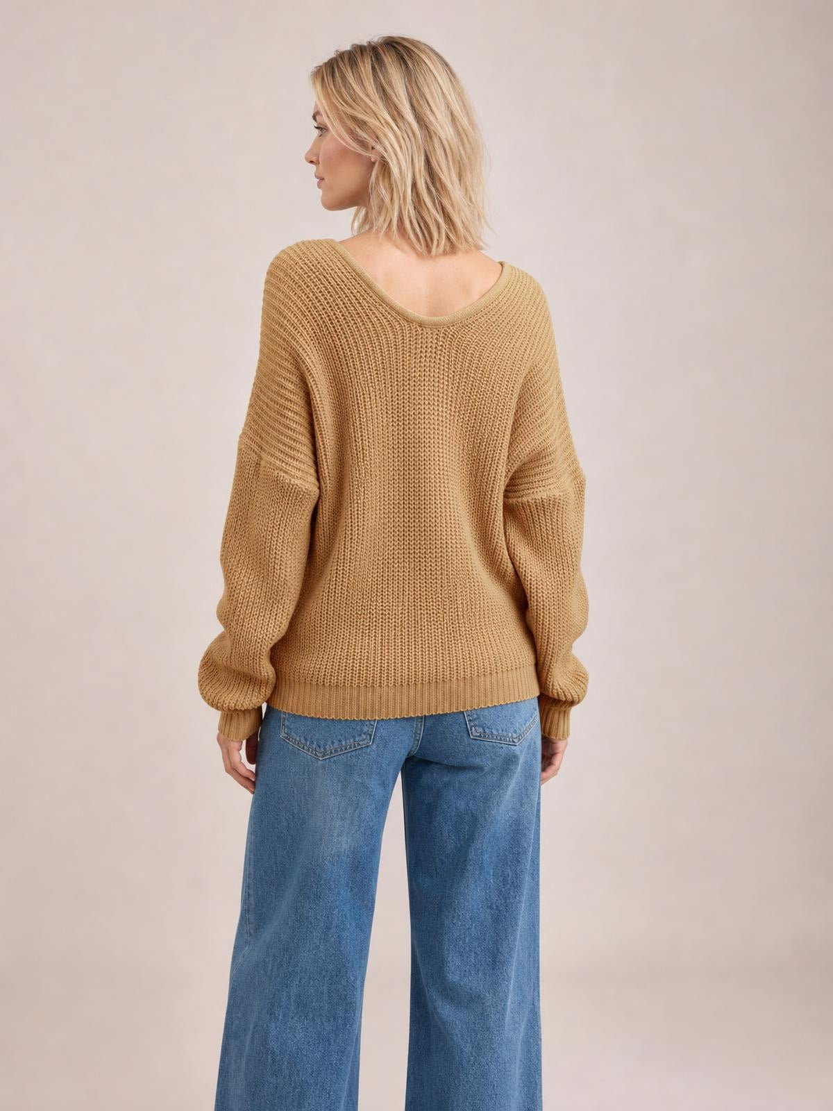 Model shown from behind wearing a camel V-neck drop shoulder sweater with a relaxed silhouette, textured knit construction, ribbed cuffs, and a ribbed hem.