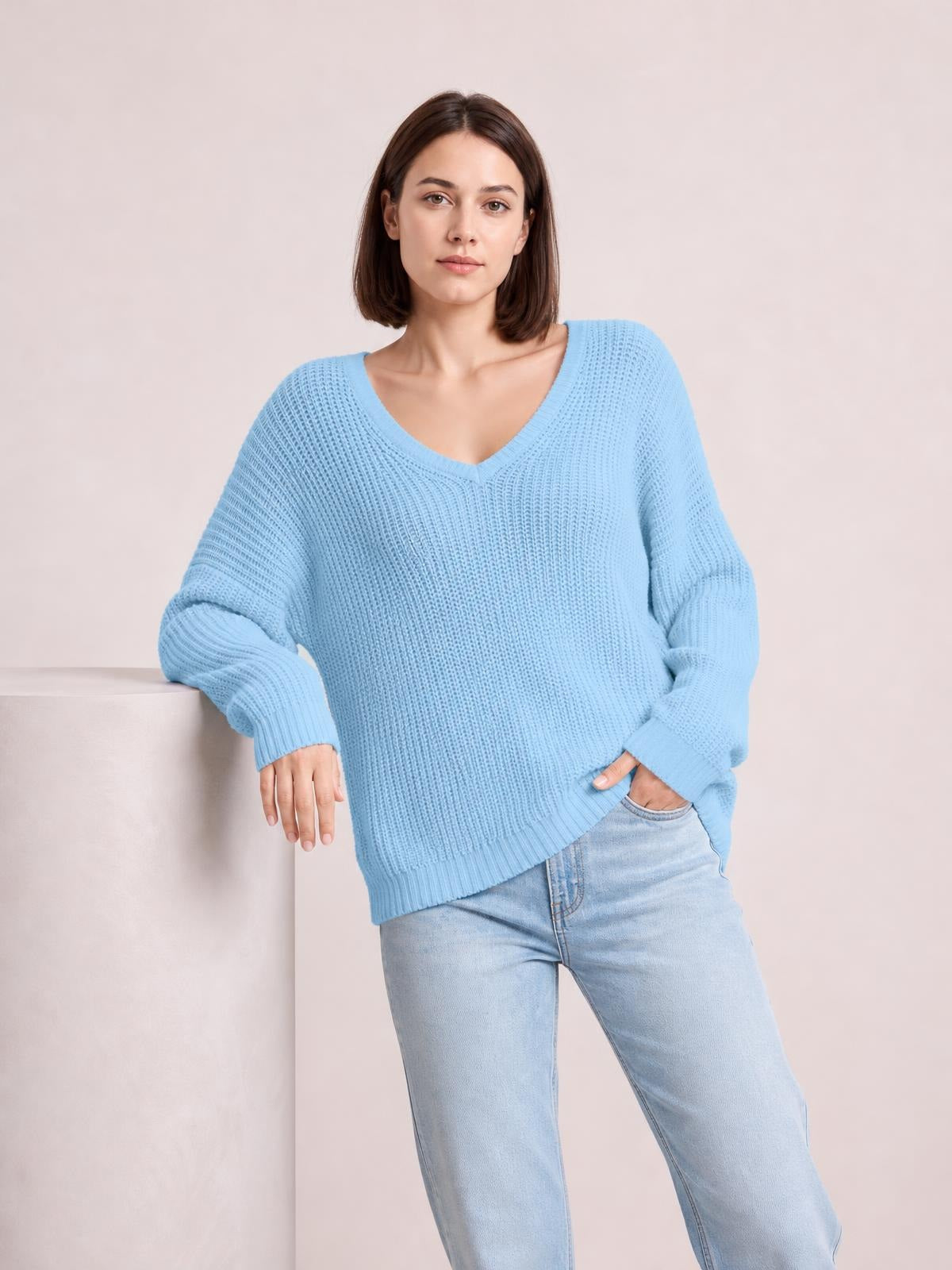 Model poses in a light blue V-neck drop shoulder sweater with a relaxed oversized silhouette, ribbed cuffs and hem, and textured knit construction.