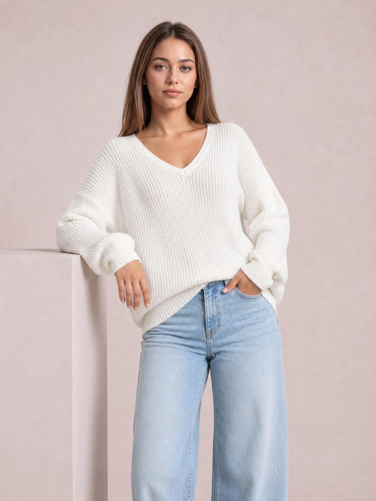 Model wearing an ivory V-neck drop shoulder sweater with a relaxed silhouette, textured knit, ribbed cuffs and hem, paired with light-wash jeans.
