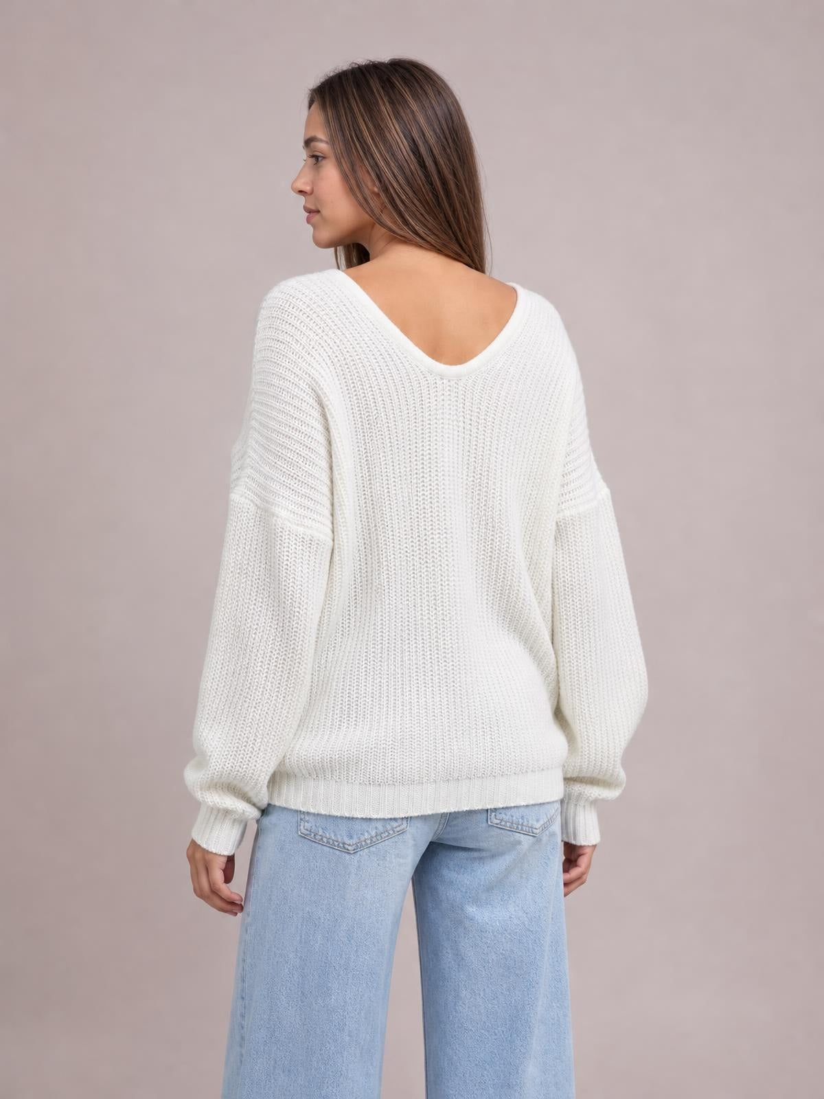 Model turned slightly to show the back of a white V-neck drop shoulder sweater with a relaxed silhouette, textured knit, and ribbed cuffs and hem.