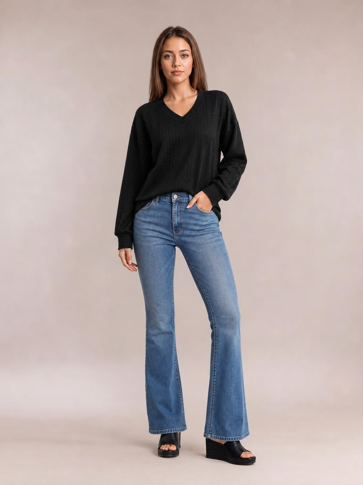 Model poses in a black V-neck dropped shoulder blouse with long sleeves, a relaxed long silhouette, and subtle textured construction.