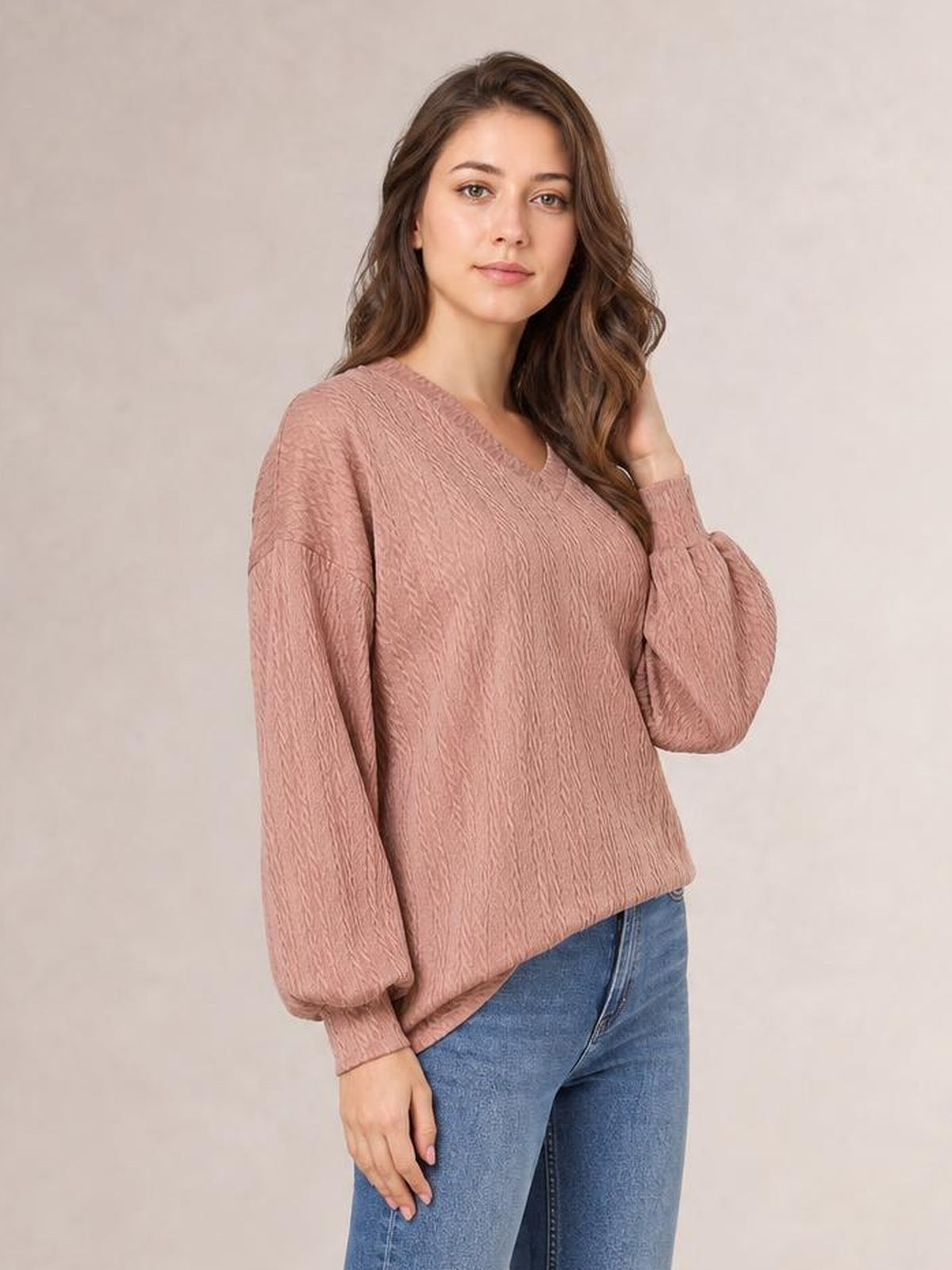 A model poses in a dusty rose V-neck dropped shoulder blouse with a relaxed long silhouette, textured fabric, long sleeves, and ribbed cuffs.