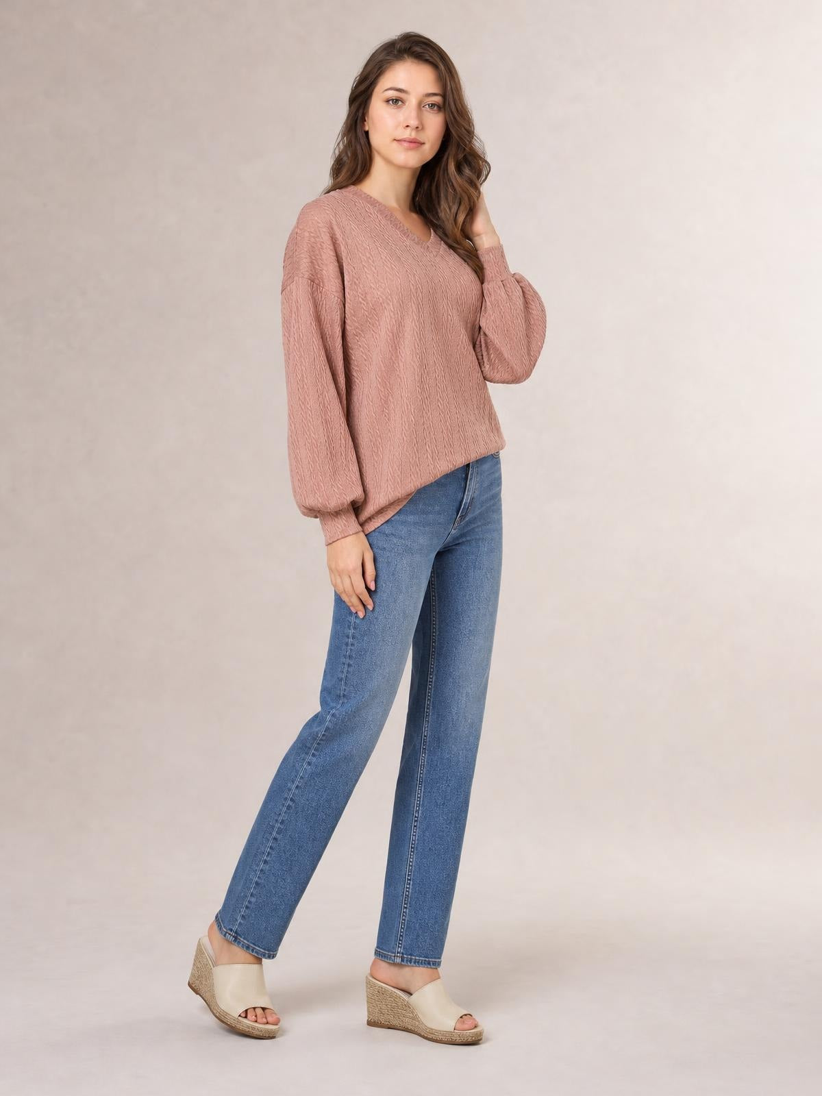 Model poses in a dusty rose V-neck dropped shoulder blouse with long sleeves, textured solid fabric, relaxed long silhouette, and ribbed cuffs.