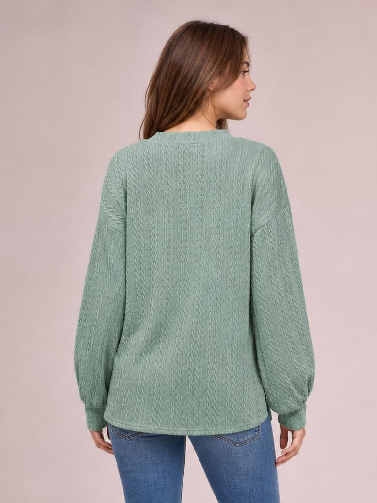 Model shown from behind wearing a sage green V-neck dropped-shoulder blouse with a long relaxed silhouette, textured fabric, long sleeves, and cuffed wrists.