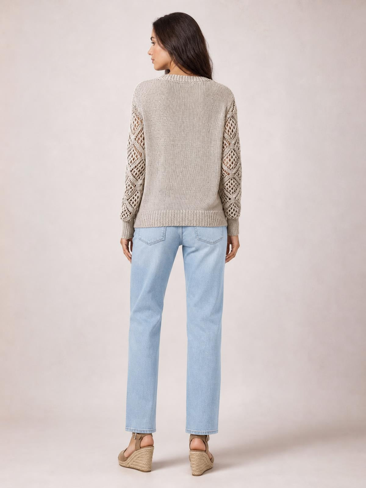 Model shown from behind wearing a taupe knit sweater with openwork hollow-out sleeves, ribbed neckline, cuffs and hem, and a relaxed straight silhouette.