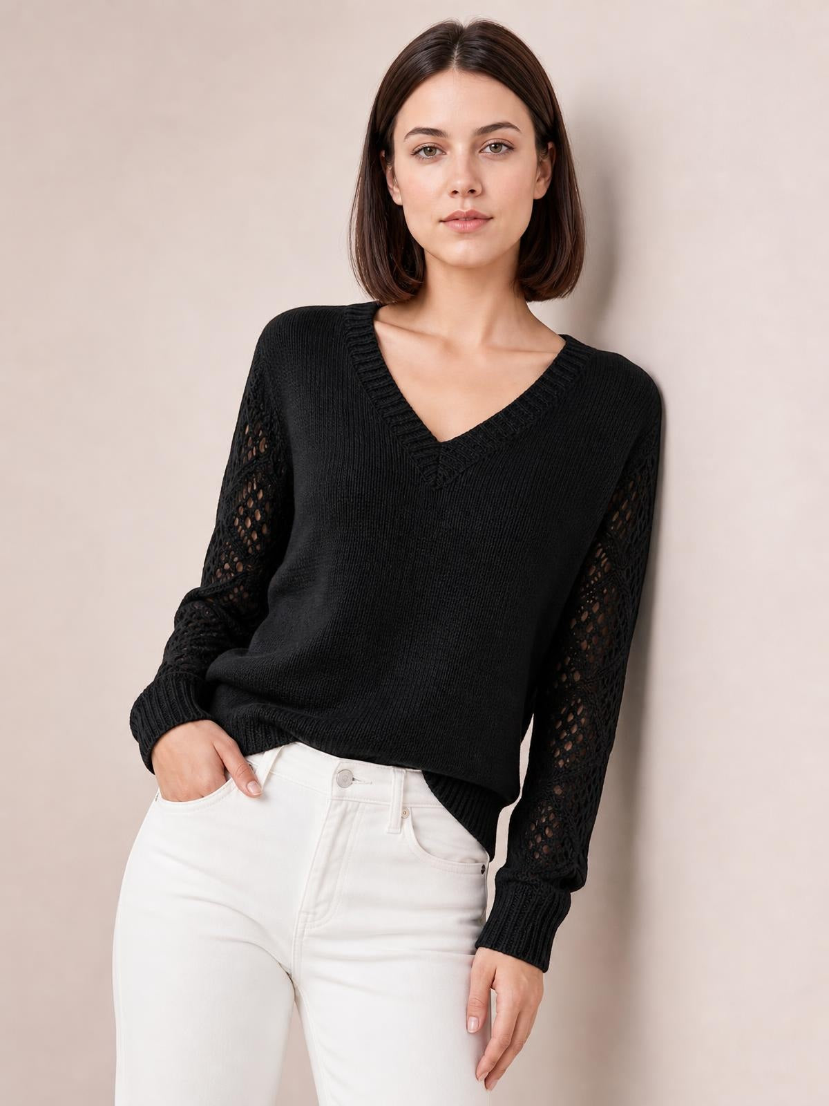 A model poses with one hand in her pocket wearing a black V-neck knit sweater with openwork hollow-out sleeves, ribbed cuffs, and a relaxed silhouette.