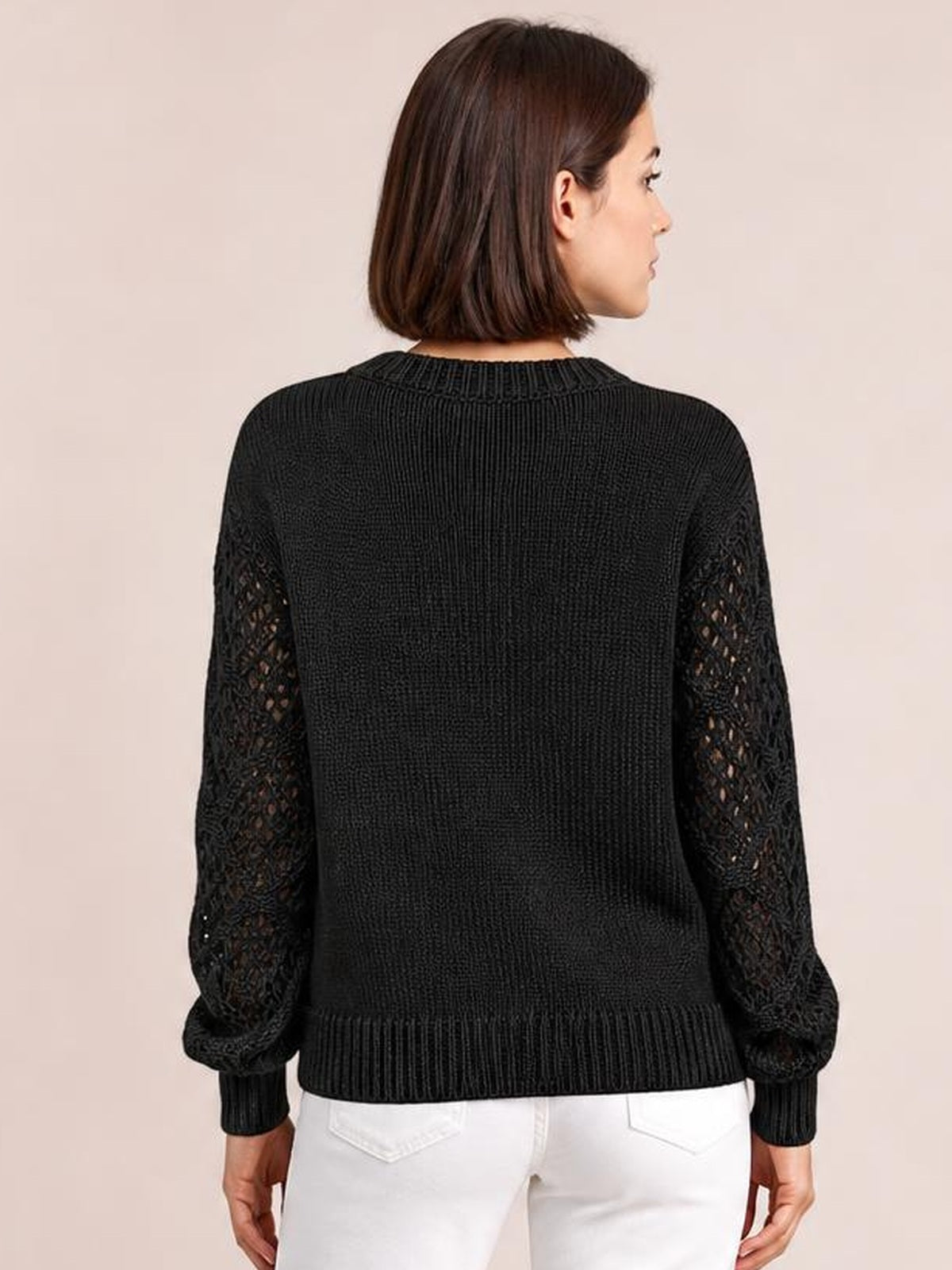 A model stands with her back to the camera in a black knit sweater with openwork sleeves, ribbed cuffs and hem, and a relaxed silhouette.