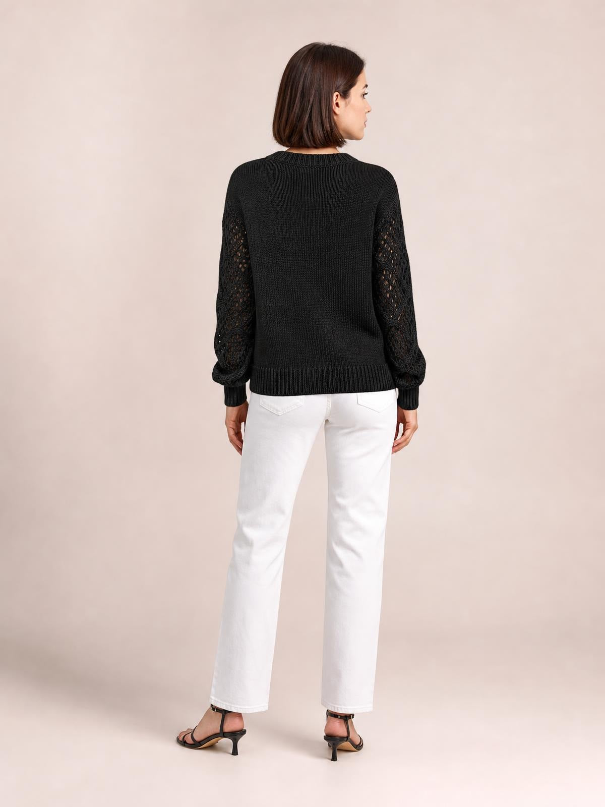 A model stands with her back turned in a black knit sweater with openwork sleeves, ribbed cuffs and hem, and a relaxed silhouette.