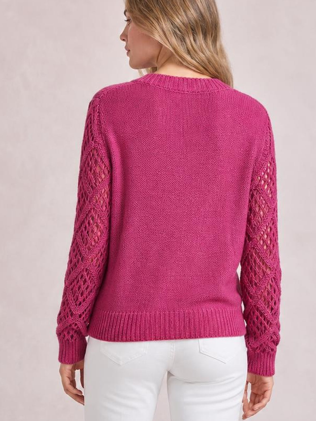 A model faces away wearing a bright magenta knit sweater with openwork sleeves, ribbed cuffs and hem, and a relaxed straight silhouette.