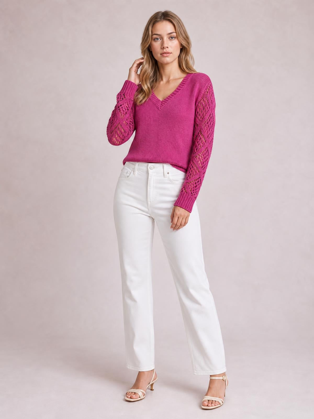 A model poses in a bright pink V-neck knit sweater with long hollow-out openwork sleeves, ribbed trim, and a relaxed straight silhouette.