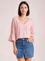 Model wears a pink V-neck lace blouse with opaque fabric, lace-trimmed sleeves, and flared flounce cuffs in a relaxed silhouette.