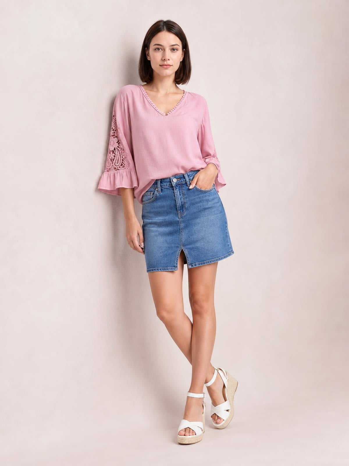 Model wears a pink V-neck lace blouse with three-quarter flounce sleeves, relaxed silhouette, and lace panel details while posing with one hand in her denim skirt pocket.
