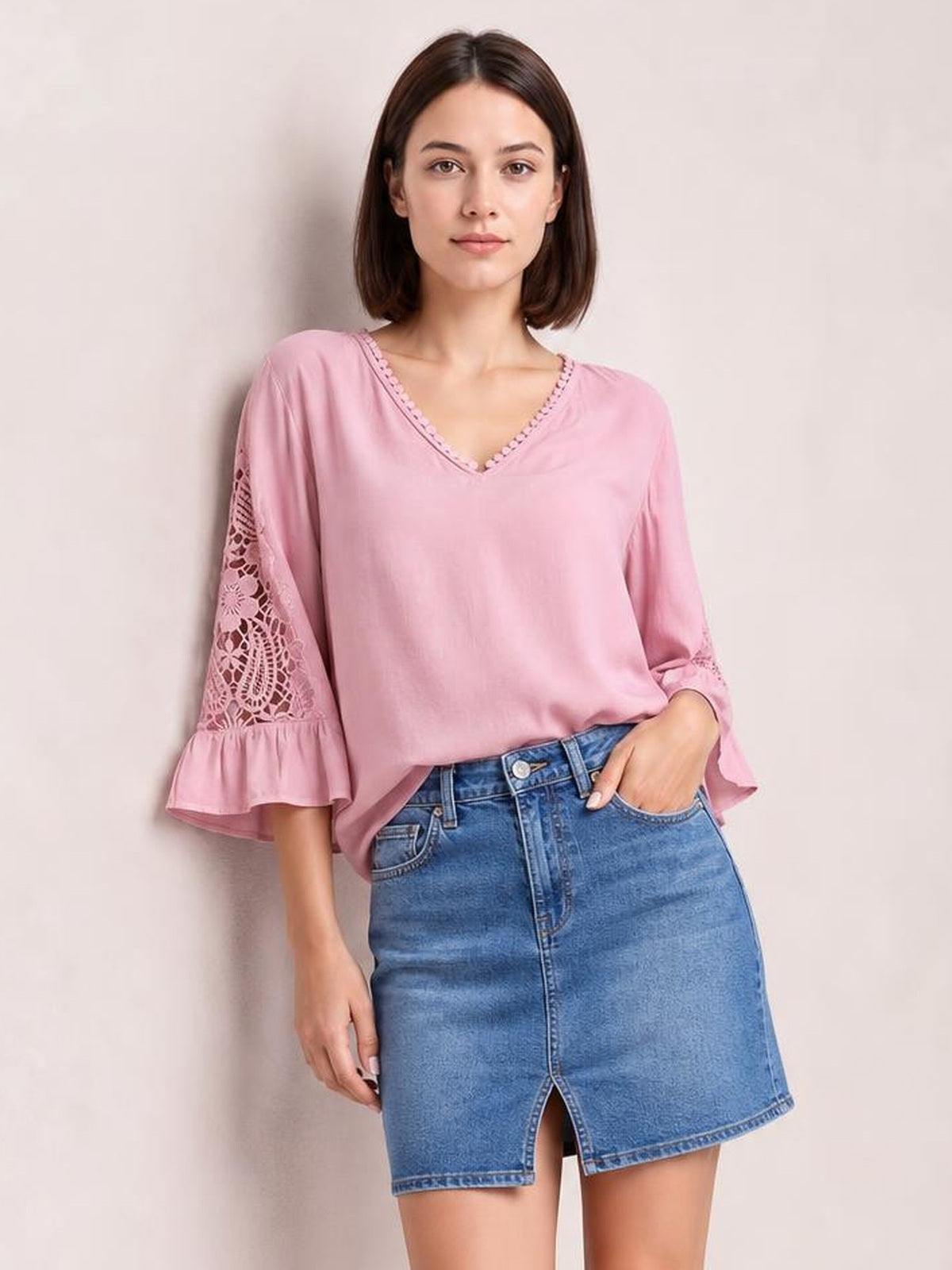 A model wears a pink V-neck lace blouse with decorative neckline trim, lace sleeve panels, flounce cuffs, and a relaxed silhouette.