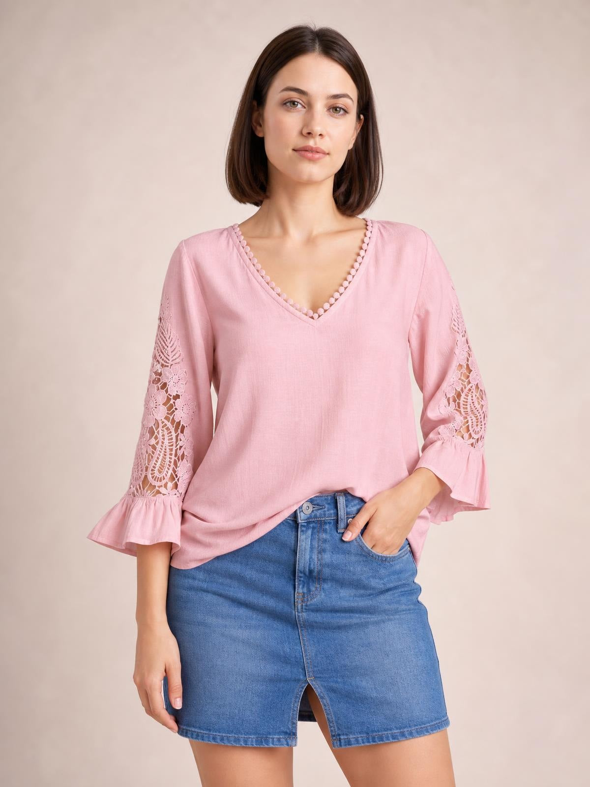 Model wearing a pink V-neck blouse with lace-inset flounce sleeves, floral cutout details, and a relaxed straight silhouette, posing with one hand in her pocket.