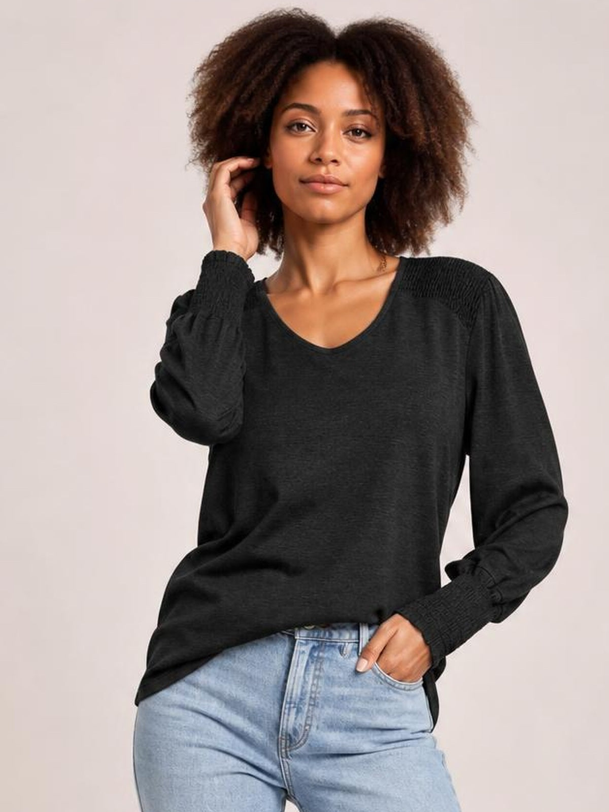 Model wearing a black V-neck t-shirt with voluminous lantern sleeves, gathered cuffs, and a relaxed silhouette while posing with one hand in her jeans pocket.